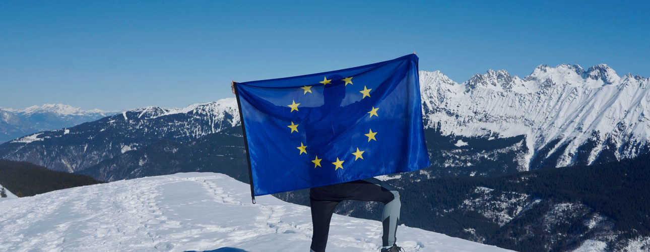 Muž mává evropskou vlajkou na vrcholu hory
