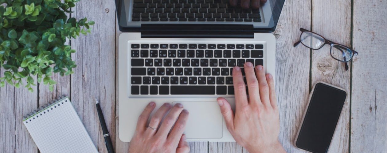 Pracovní stůl copywritera s notebookem, zápisníkem, perem, telefonem, brýlemi a rostlinou v květináči